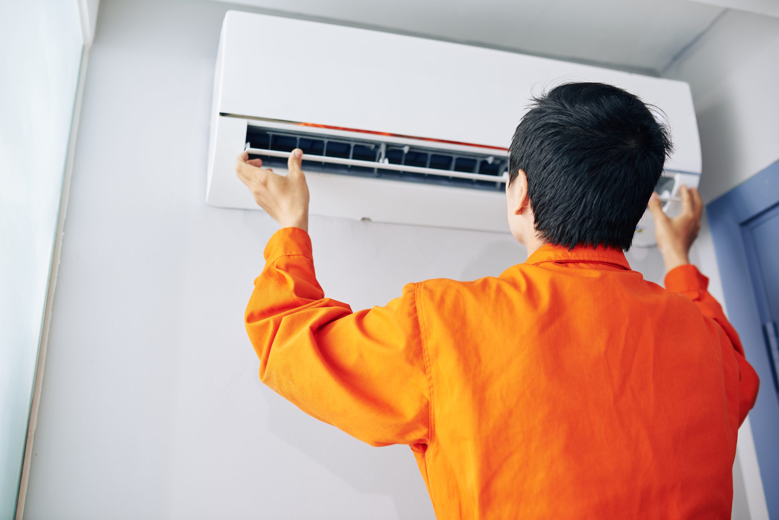 Installing air conditioner Repairman in orange uniform installing or checking air conditioner in apartment of client